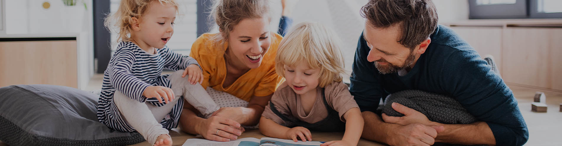 Young parents help their children learn to read while enjoying an afternoon in their brightly-lit living room