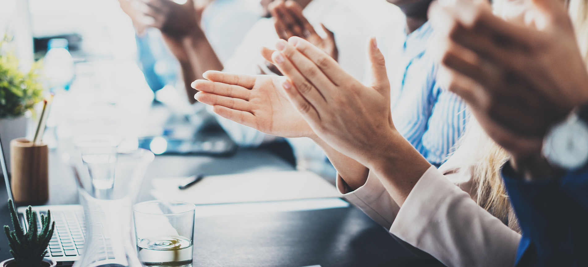Various sets of hands clapping at a meeting table.