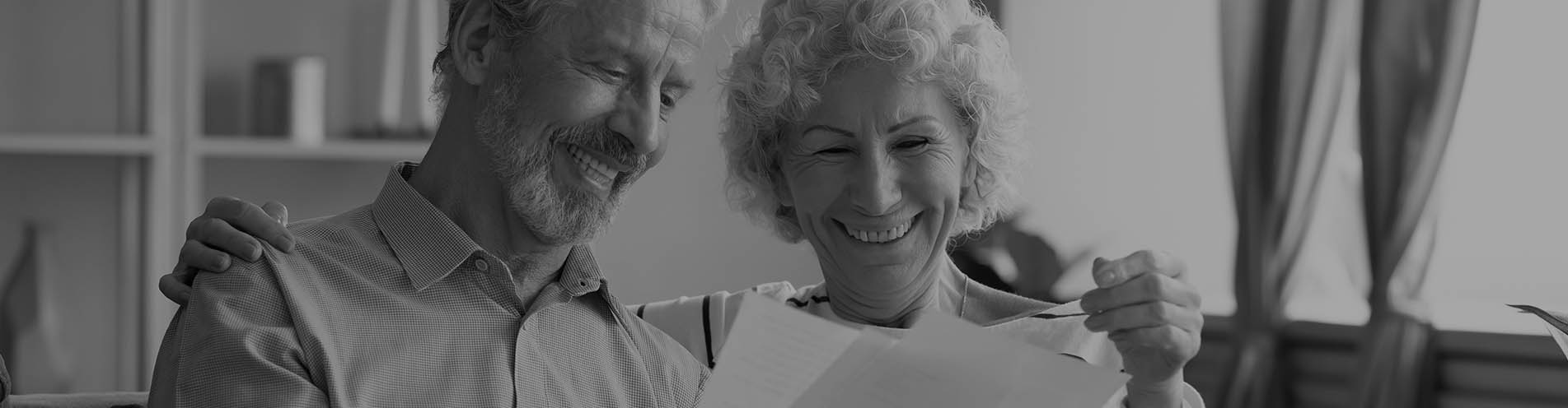 A happy older couple looking at printed documents in a brightly-lit room in their home